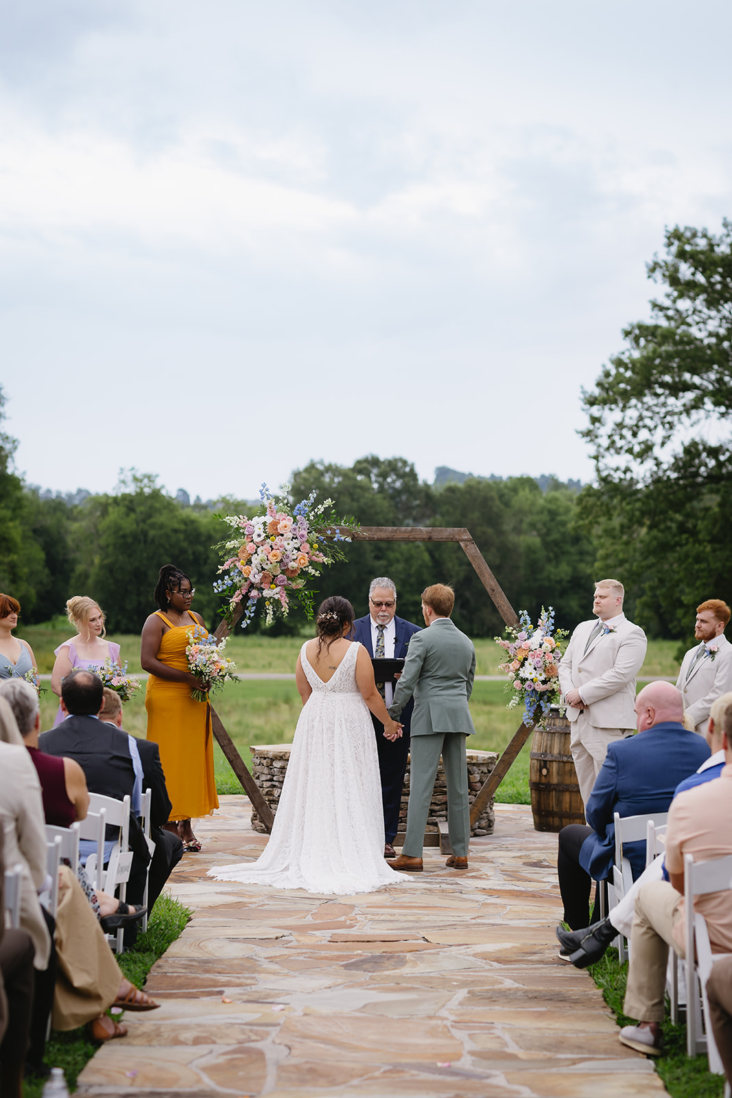 Meredith & Benjamin exchange vows under a floral hexagon arch on the Patio field at Covey Creek