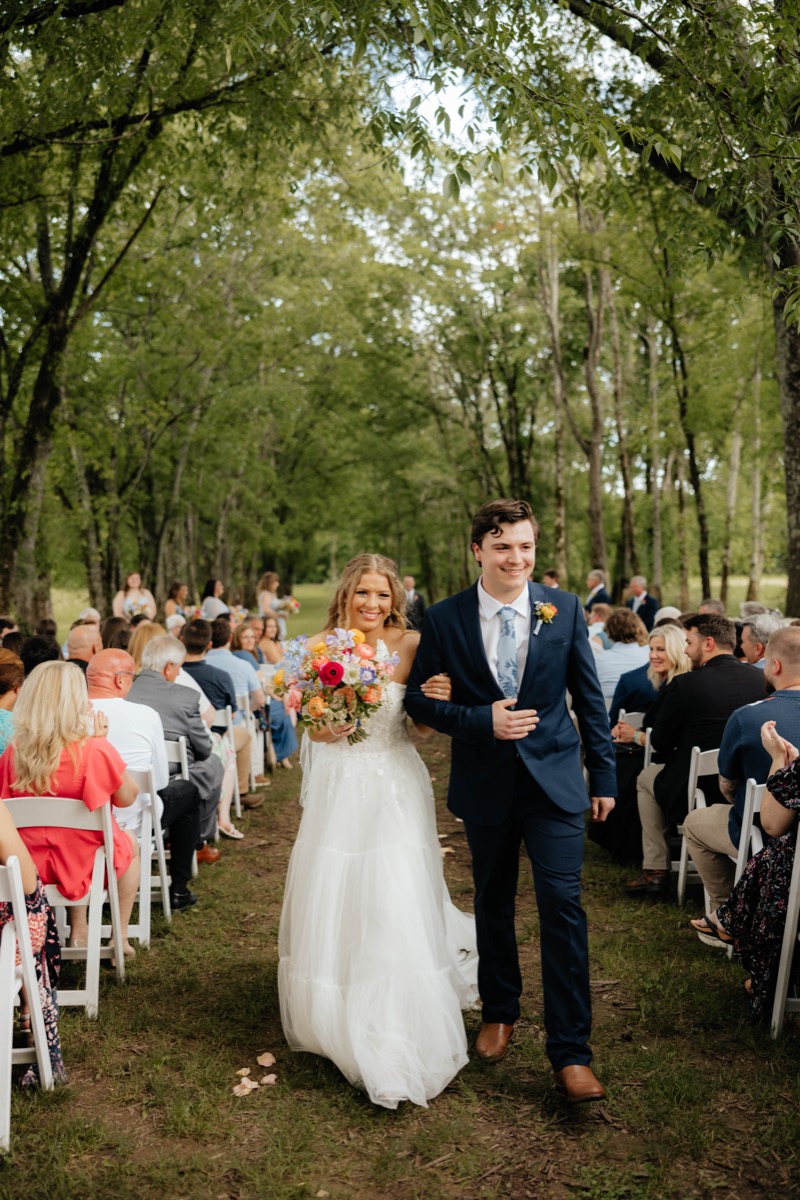 Morgan & Caden recess arm-in-arm down Covey Creek’s Tunnel of Love aisle, colorful bouquet in her hands