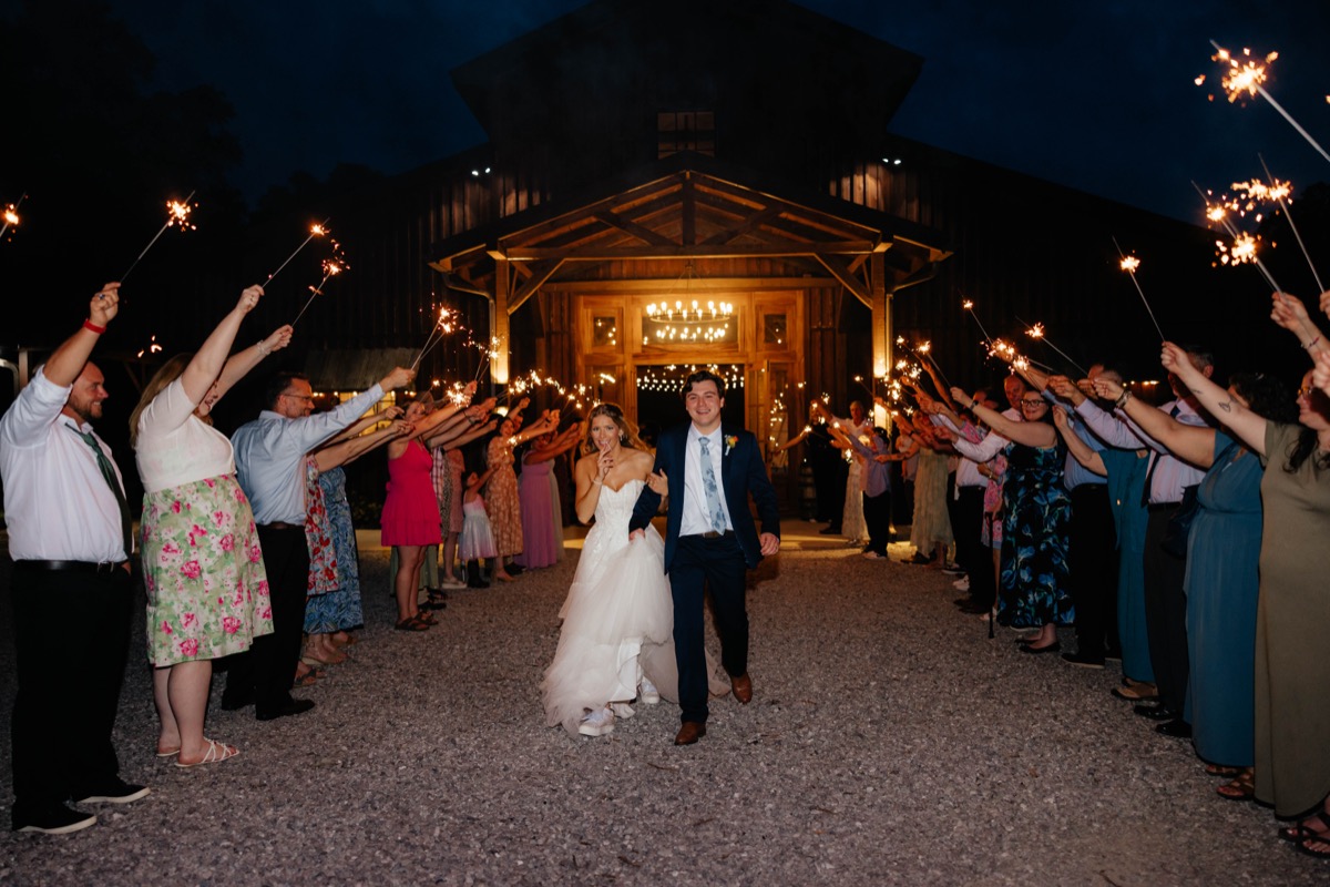 Morgan & Caden walk a sparkler send-off path at Covey Creek, barn entry and guests glowing behind them