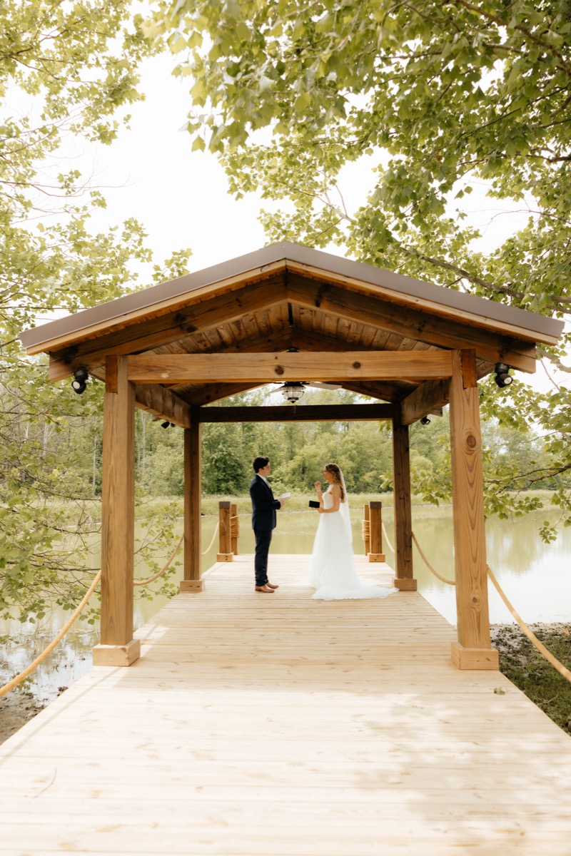 Morgan & Caden exchange vows under the timber Pond pavilion at Covey Creek, dock and trees framing them