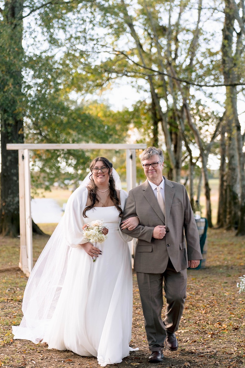 Peyton walks the leaf-strewn aisle with her father at Peyton & Jackson's outdoor Covey Creek wedding.