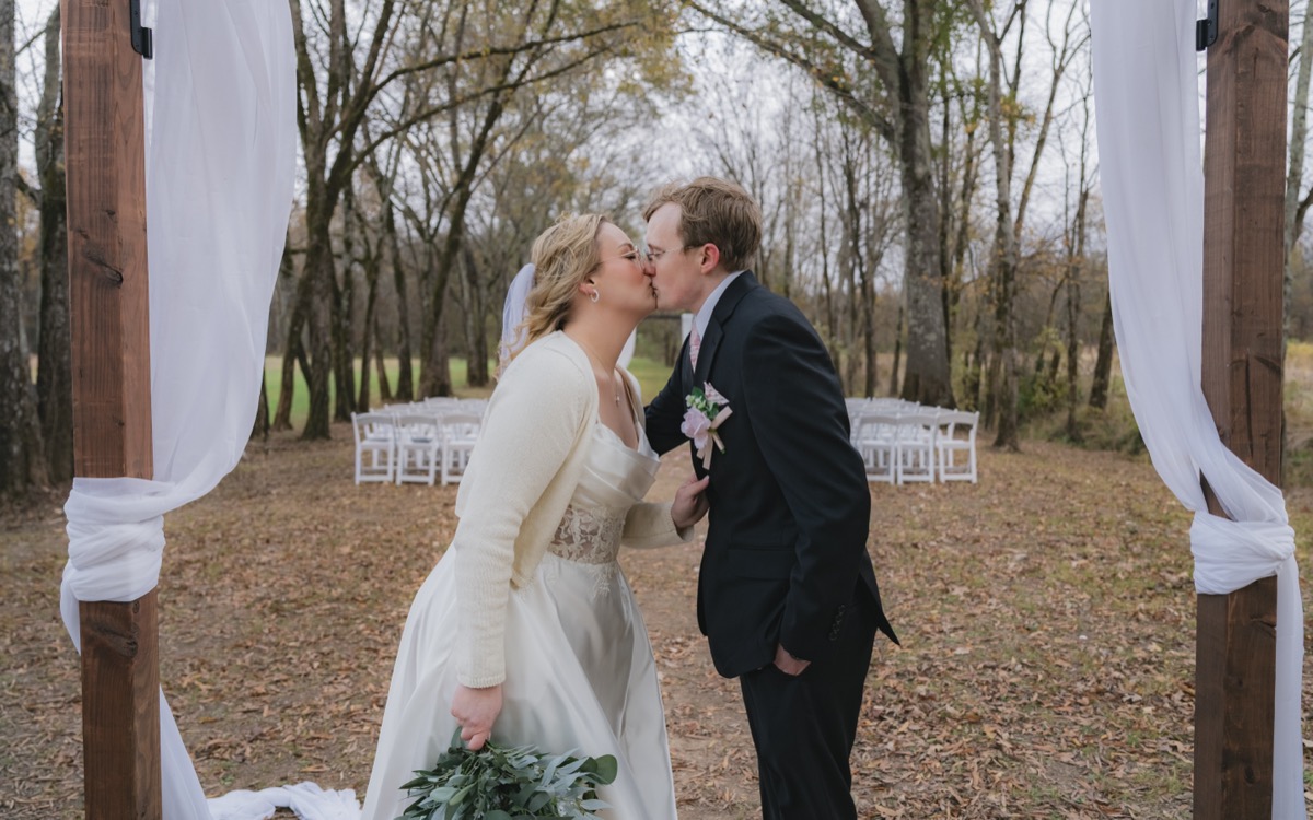 Rae & David share a kiss under white fabric at their Tunnel of Love outdoor ceremony at Covey Creek