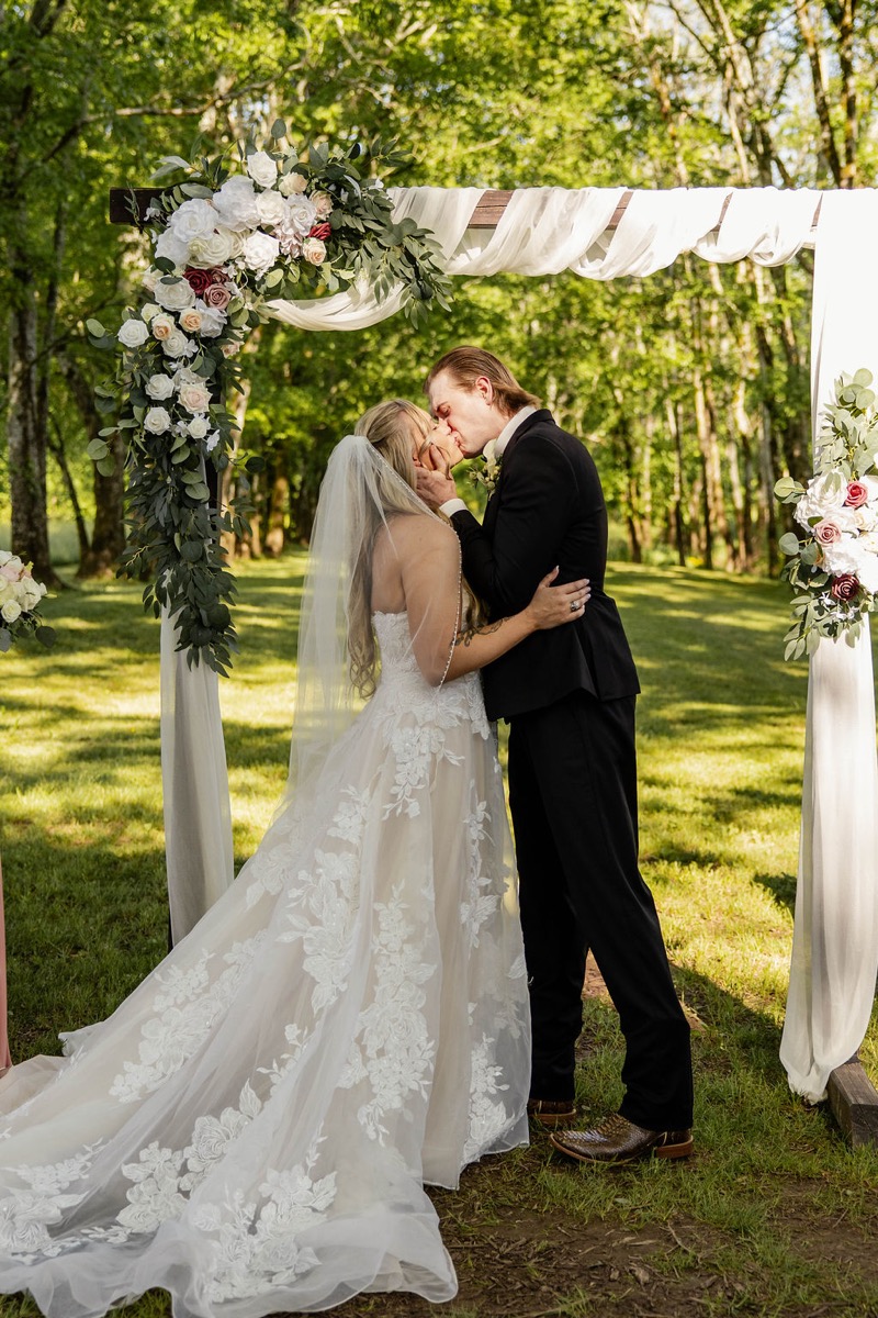 Raven & Jackson share a kiss under a fabric-draped floral arbor at their Covey Creek ceremony