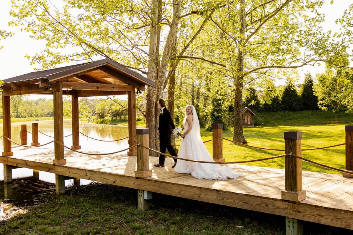 Raven & Jackson walk hand-in-hand along the wooden Pond dock at Covey Creek, her train trailing