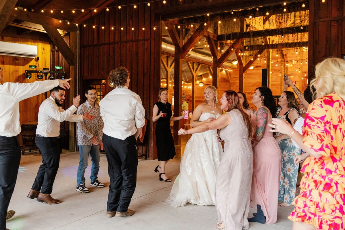 Raven & Jackson dance with guests under Edison string lights in the Covey Creek reception barn