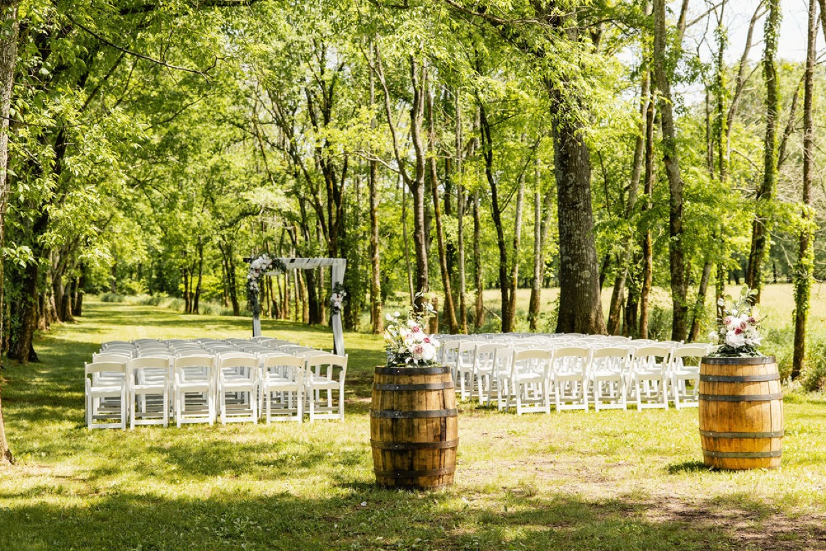 Outdoor ceremony aisle for Raven & Jackson at Covey Creek with floral barrels, white chairs, and a draped wooden arbor
