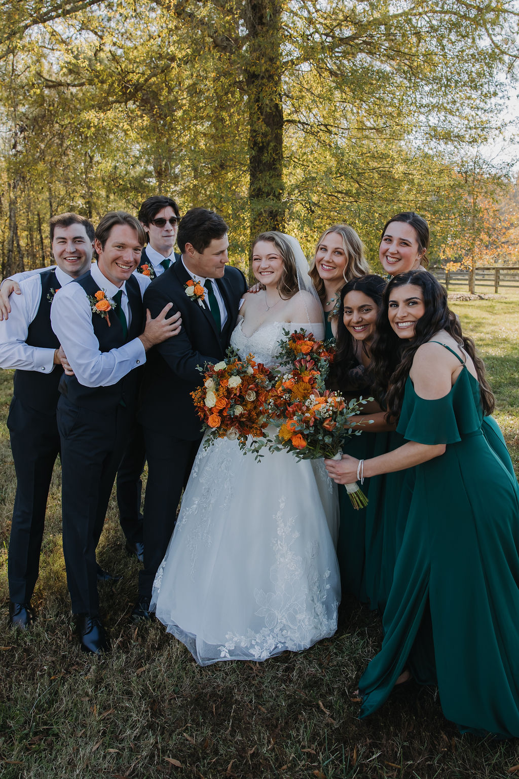 Rebecca & Troy pose with green-dressed bridesmaids and vested groomsmen in a sunny field at Covey Creek.