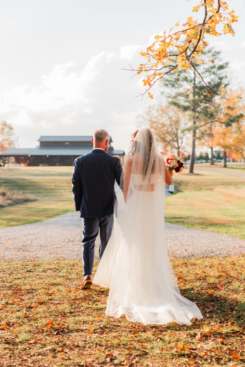 Sarah & Adam walk a leaf-strewn gravel path toward the barn after their Covey Creek ceremony