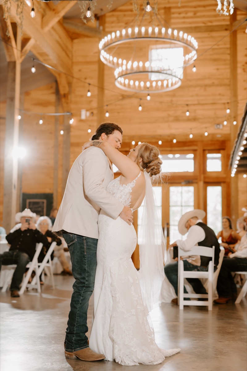 Shay & Wyatt share their first dance under a glowing chandelier in the rustic barn reception at Covey Creek.