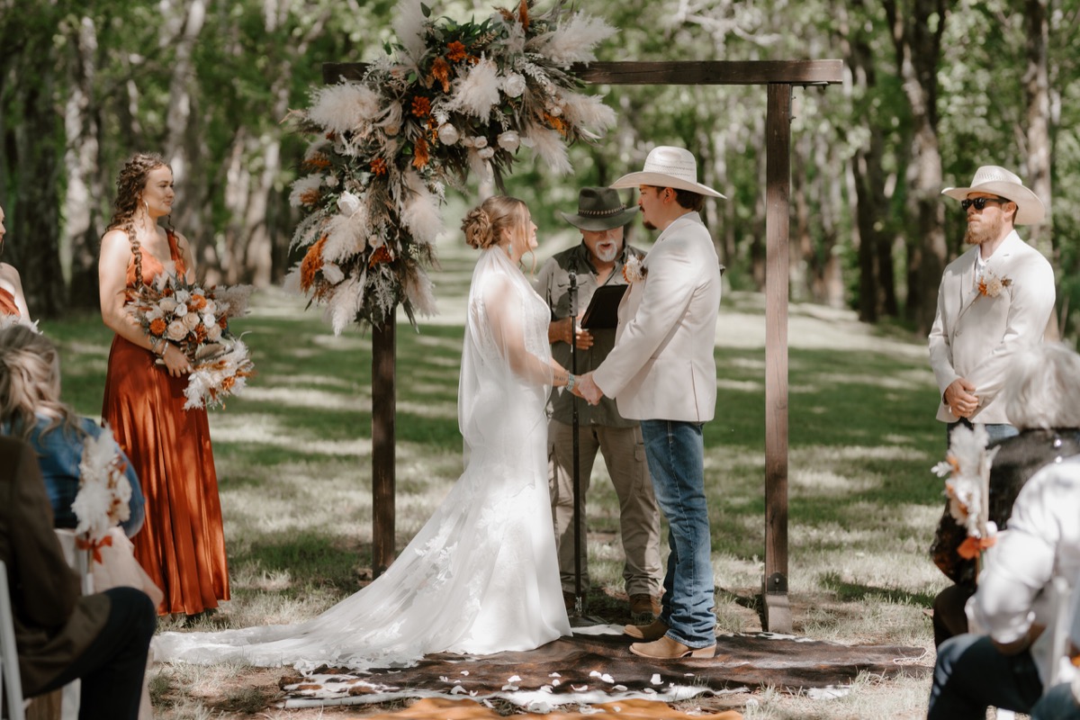 Shay & Wyatt hold hands under a pampas-draped wooden arbor during their wooded ceremony at Covey Creek.