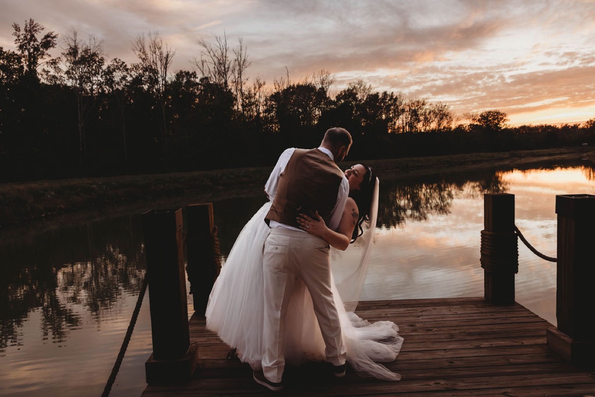 Tim dips Tori for a kiss on the wooden Pond dock under a fiery orange sunset sky at Covey Creek