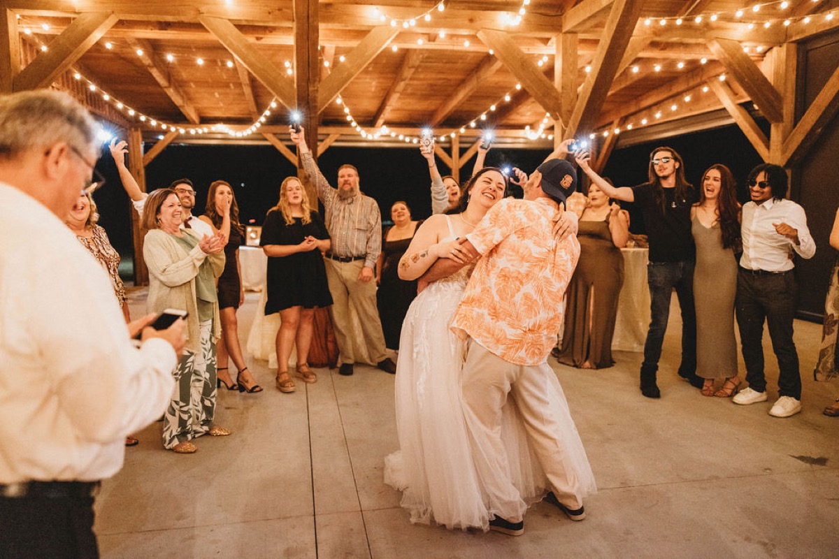 Tori & Tim hug under Patio string lights as guests raise phone flashlights at Covey Creek reception