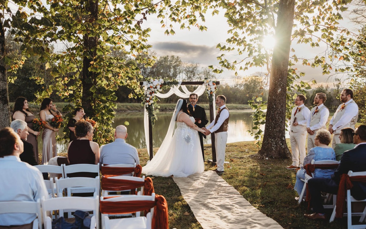 Tori & Tim exchange vows under a floral arbor by the Pond with seated guests at Covey Creek