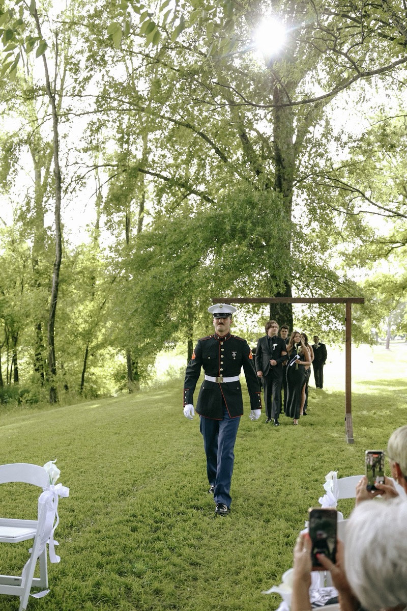Brody in Marine dress blues walks the grassy aisle toward Cadence & Brody's wood arch at Covey Creek