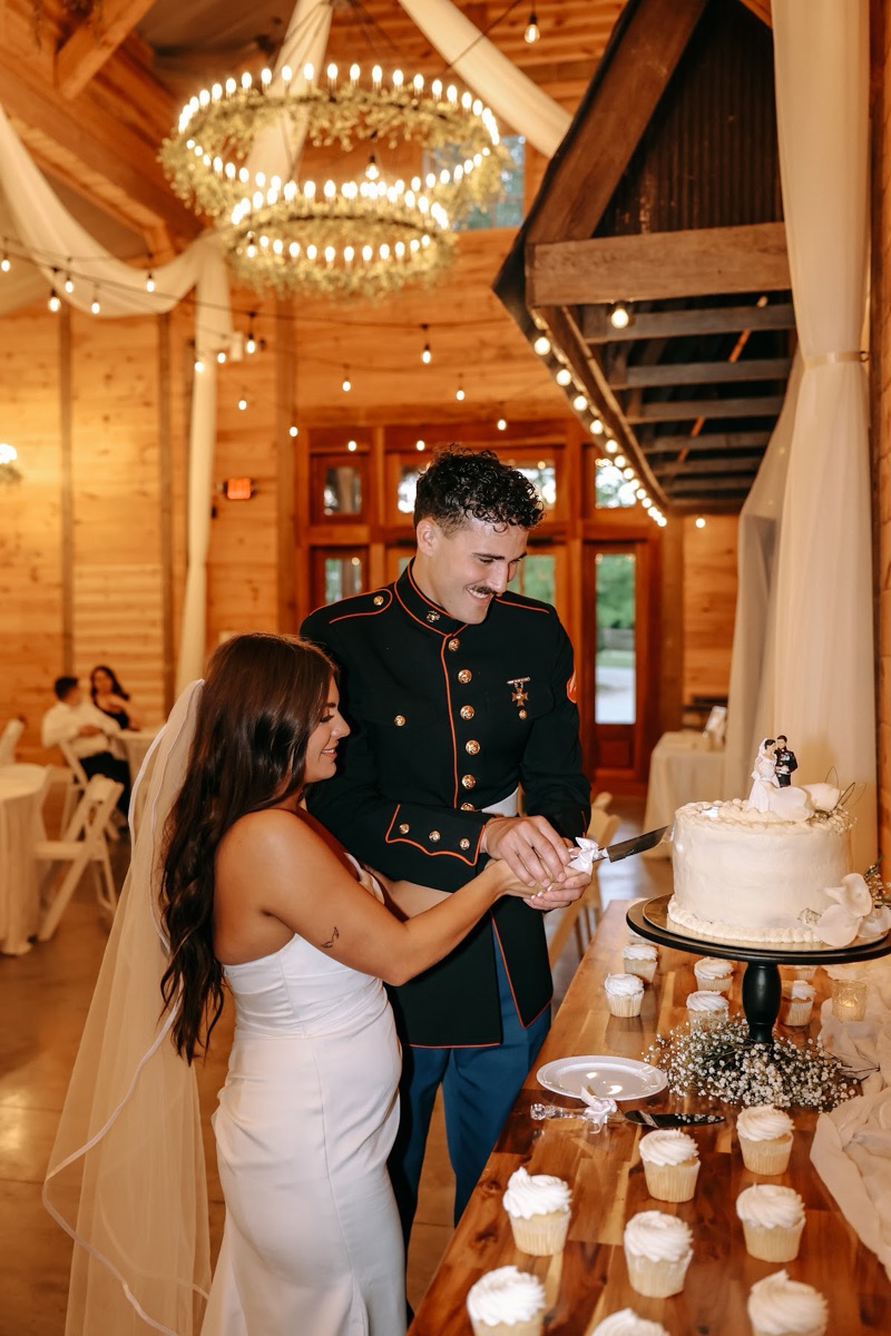 Cadence & Brody cut a white cake among cupcakes under barn chandeliers and string lights at Covey Creek
