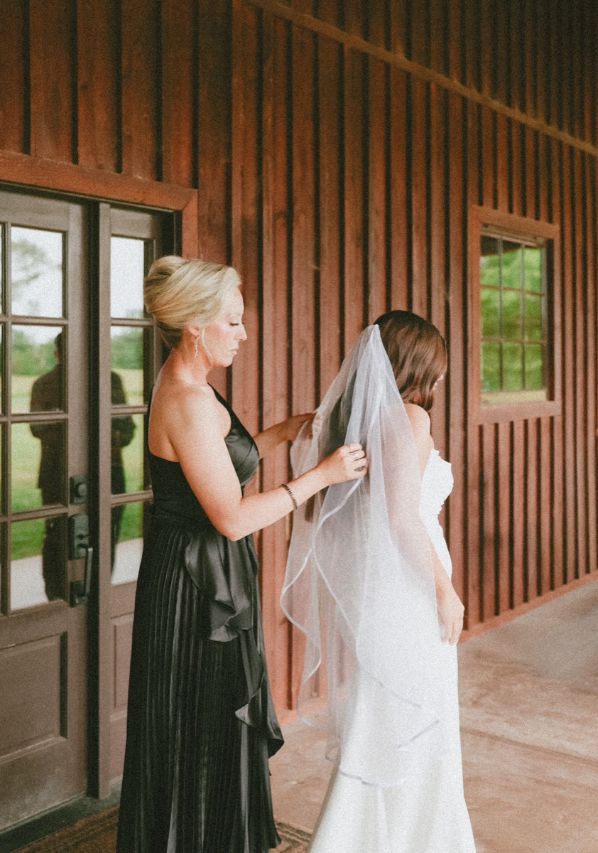 A bridesmaid settles Cadence's veil by the wood-slat barn doors for Cadence & Brody at Covey Creek