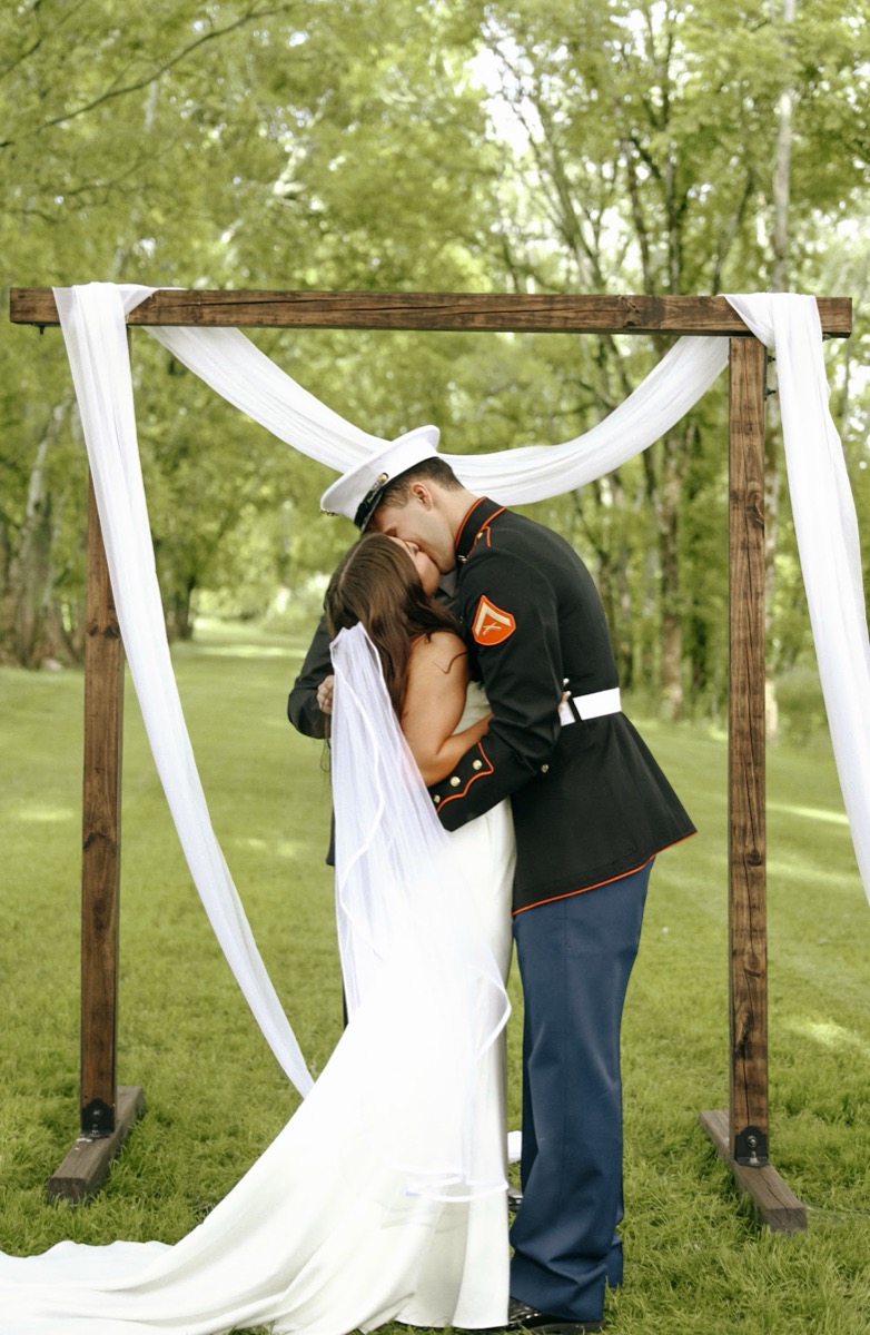 Cadence & Brody share their first kiss under a fabric-draped wood arch on the lawn at Covey Creek