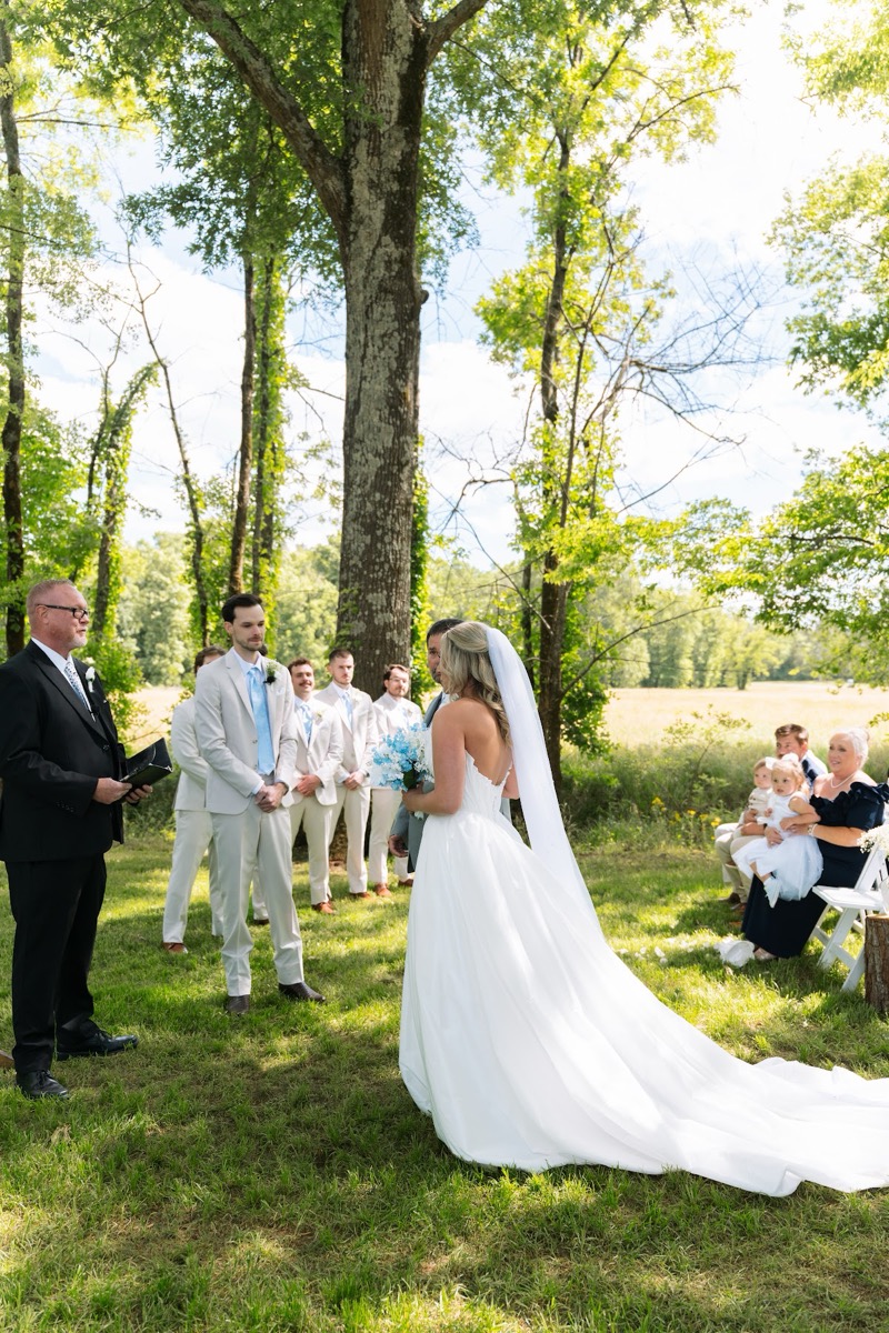 Kyley & Nick stand under a tree canopy as guests watch their Tunnel of Love ceremony at Covey Creek