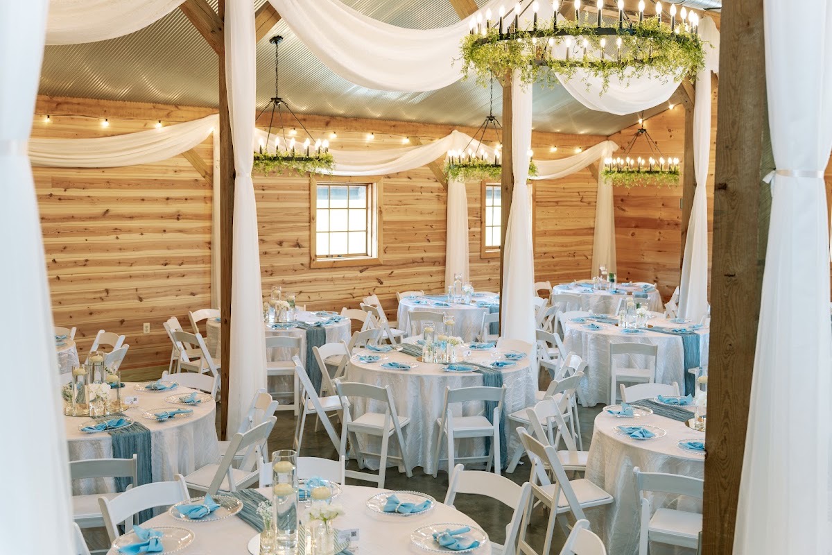 Round tables with blue runners fill the draped barn under greenery chandeliers for Kyley & Nick at Covey Creek