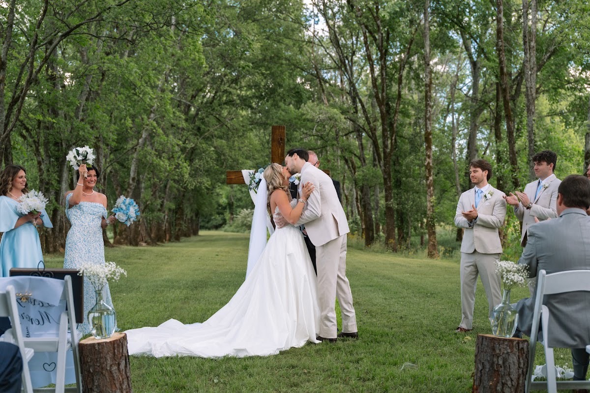 Kyley & Nick share their first kiss before a floral wooden cross as guests cheer at Covey Creek