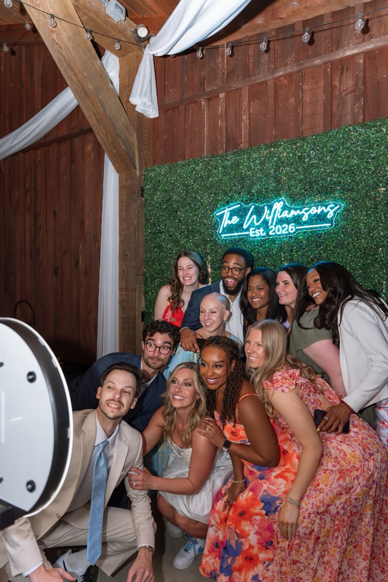 Kyley & Nick pose with friends by a neon Williamsons sign at their barn reception at Covey Creek