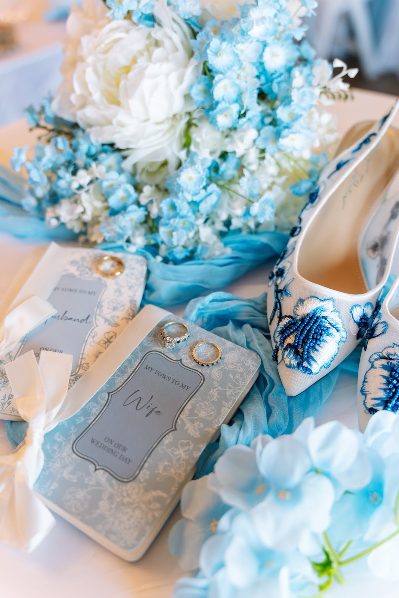 Blue-embroidered heels, vow books, and rings flat-lay with peonies for Kyley & Nick at Covey Creek