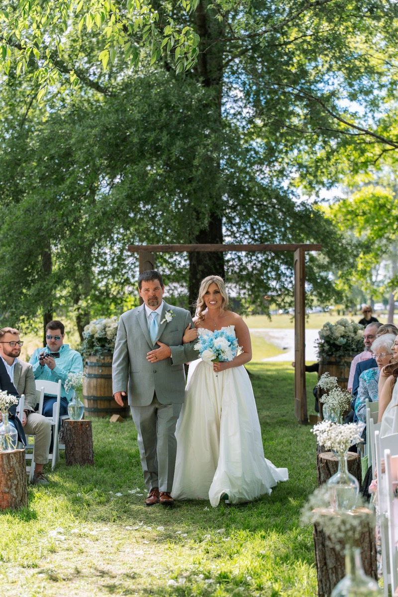 Kyley walks the petal aisle with her father for Kyley & Nick's ceremony past barrels at Covey Creek