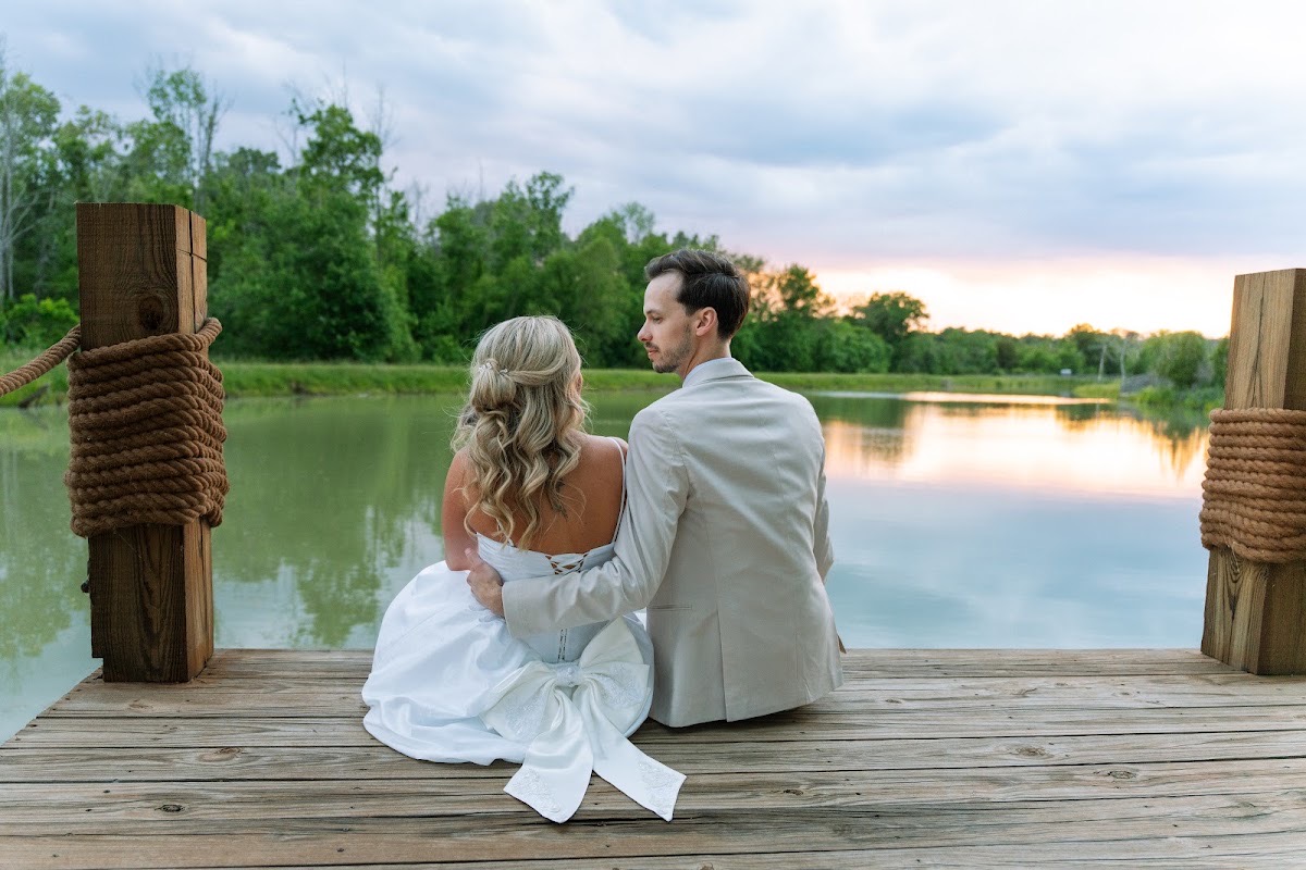 Kyley & Nick sit close on the Pond dock overlooking sunset trees after their wedding at Covey Creek