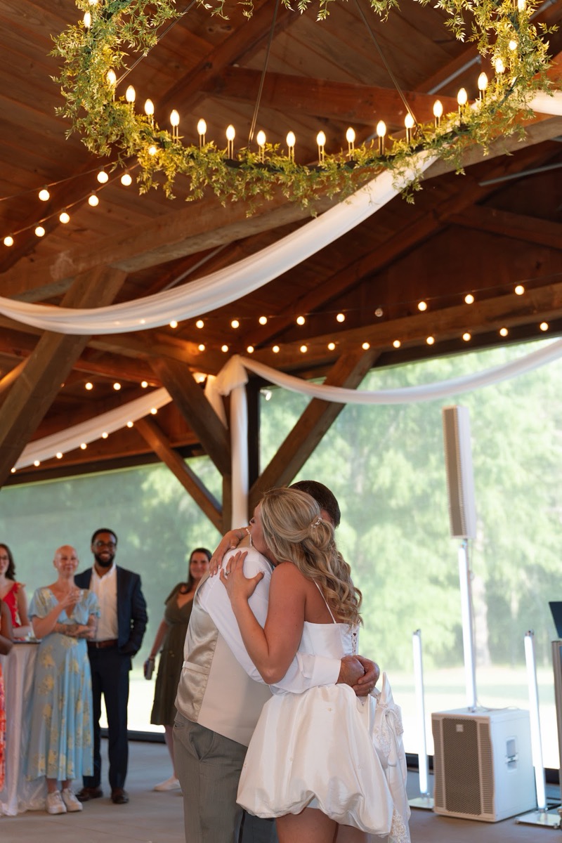 Kyley & Nick share a close hug under a greenery chandelier in the open pavilion at Covey Creek