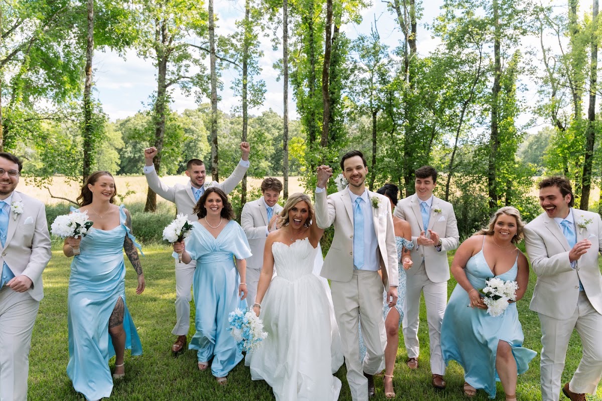 Kyley & Nick cheer with their wedding party walking the shaded lawn after vows at Covey Creek