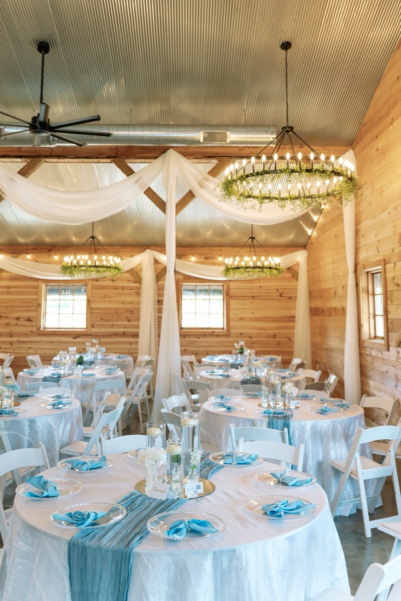 Candle centerpieces and blue runners fill the wood-walled barn for Kyley & Nick's reception at Covey Creek