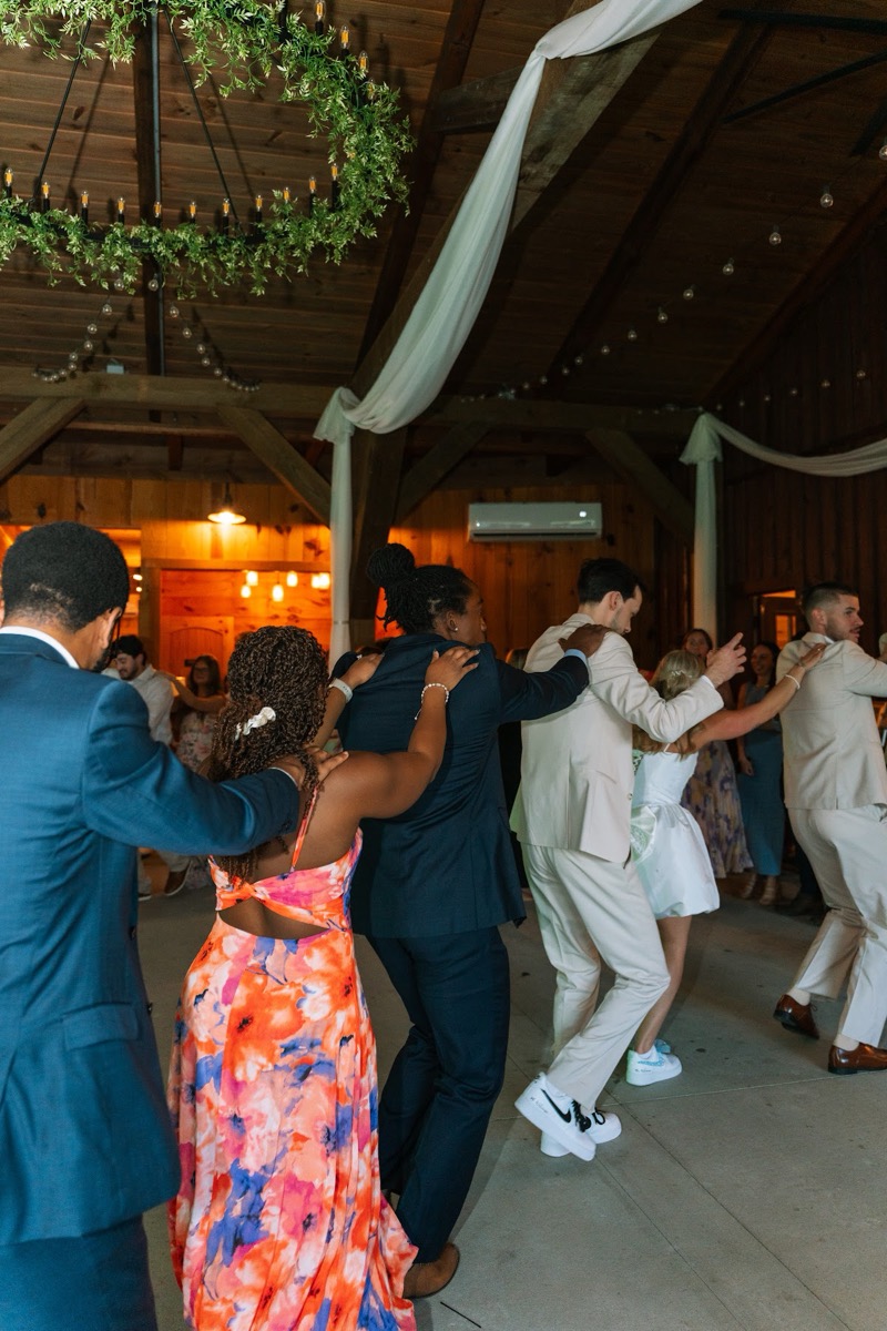 Kyley & Nick lead a conga line across the barn dance floor under chandeliers at Covey Creek
