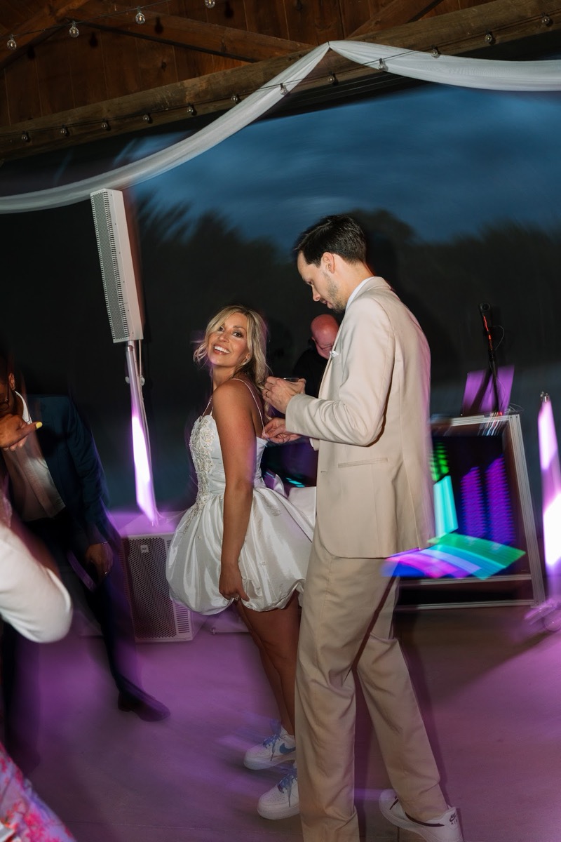 Kyley & Nick dance as she glances back in a short white reception dress under party lights at Covey Creek