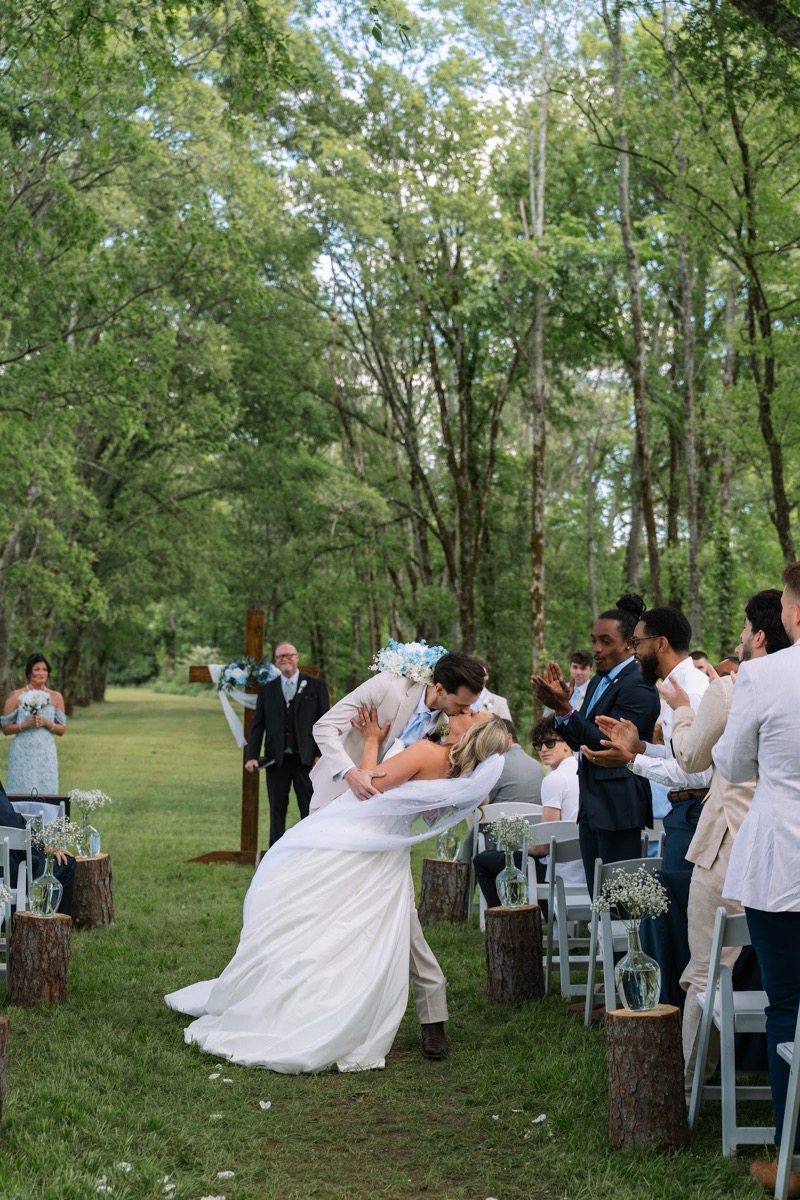 Kyley & Nick share a dip kiss down the grassy aisle as guests clap at their Covey Creek ceremony