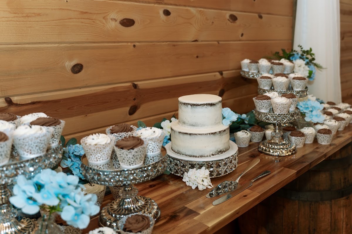 Semi-naked cake with blue bloom and cupcakes on a wood dessert table for Kyley & Nick at Covey Creek
