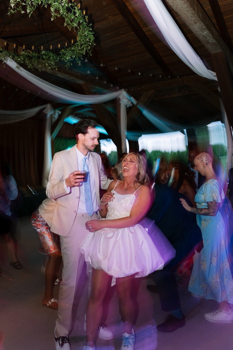 Kyley & Nick laugh on the dance floor under draped beams and colorful party lights at Covey Creek