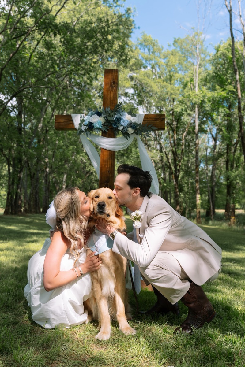Kyley & Nick kiss their golden retriever before the floral wooden cross altar at Covey Creek