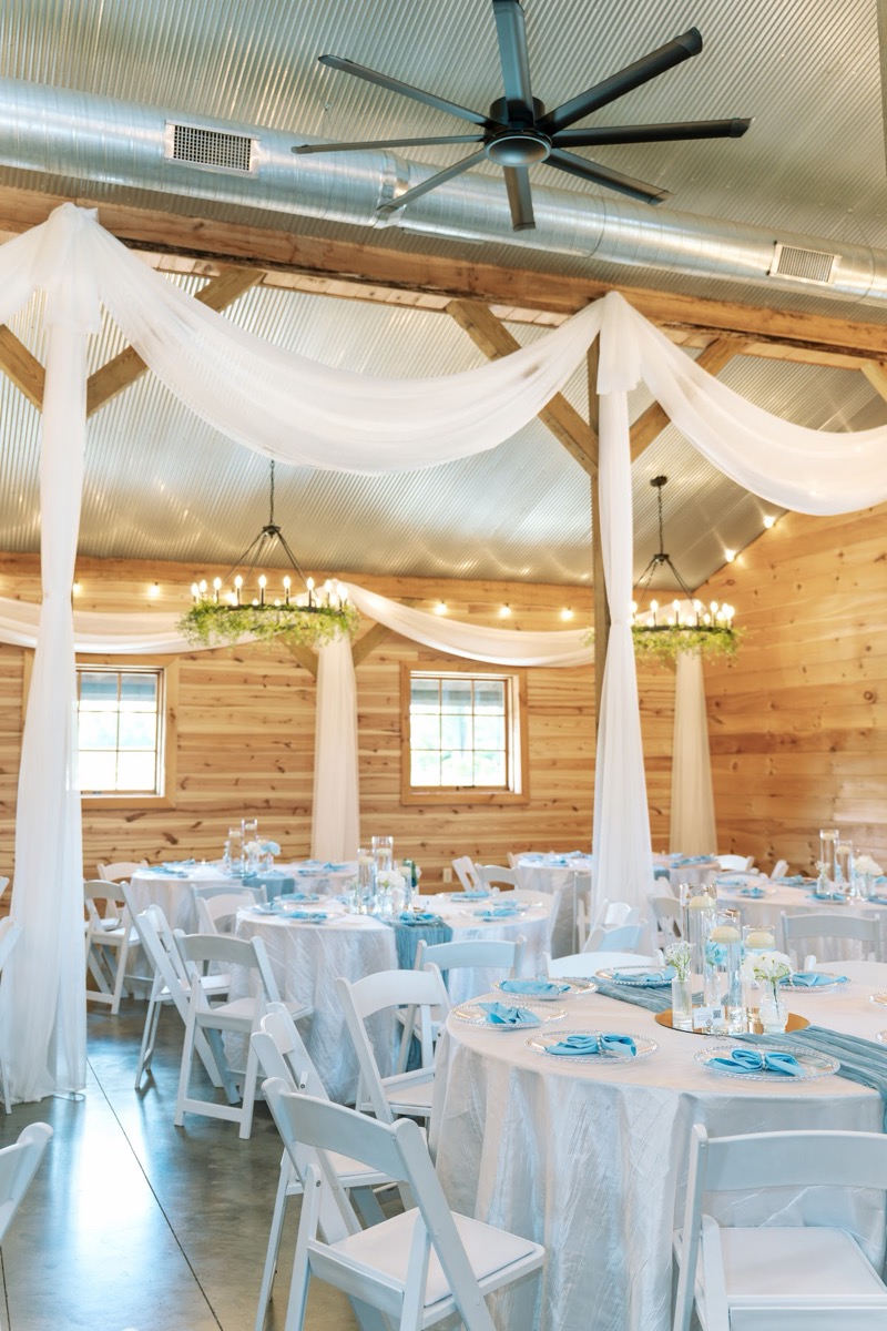 Blue-runner tables sit under white drapes and greenery chandeliers in the barn for Kyley & Nick at Covey Creek