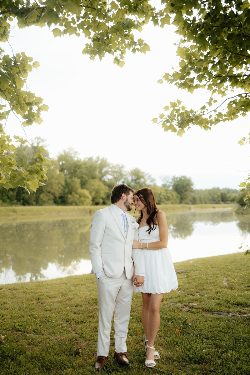 Kylie & Mason stand forehead to forehead by the Pond at Covey Creek in bright spring leaf light