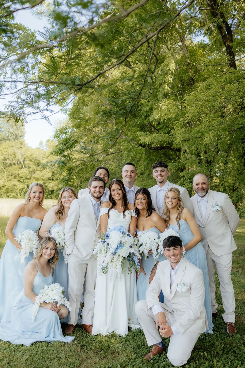 Kylie & Mason and their wedding party pose under lush spring trees on the lawn at Covey Creek