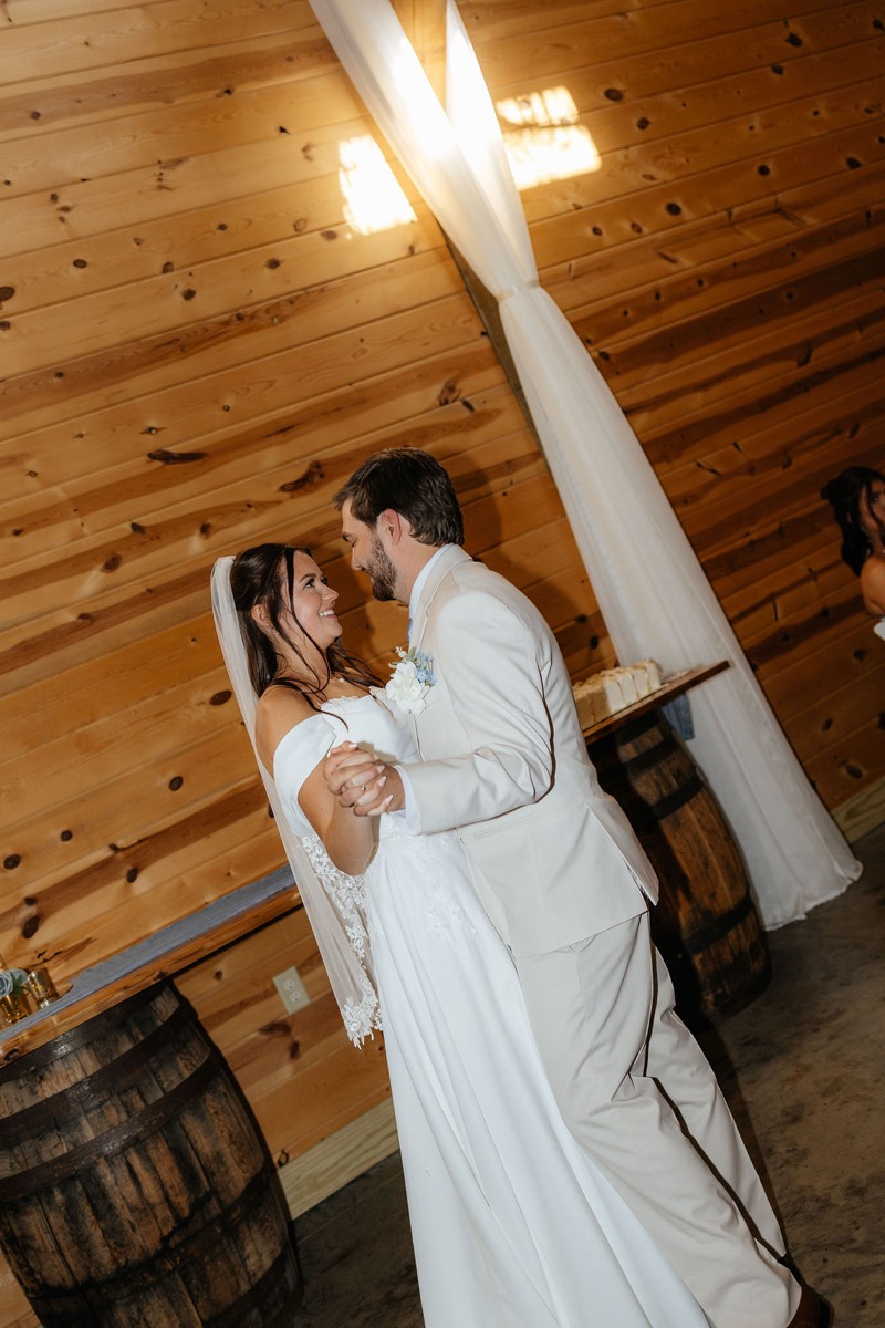 Kylie & Mason share a first dance by wood barrels in the warm indoor reception at Covey Creek