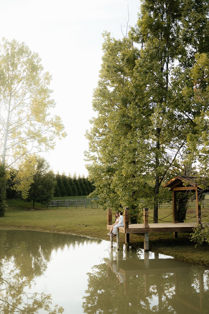 Kylie & Mason sit on the wooden dock over the calm Pond at Covey Creek in lush spring green light