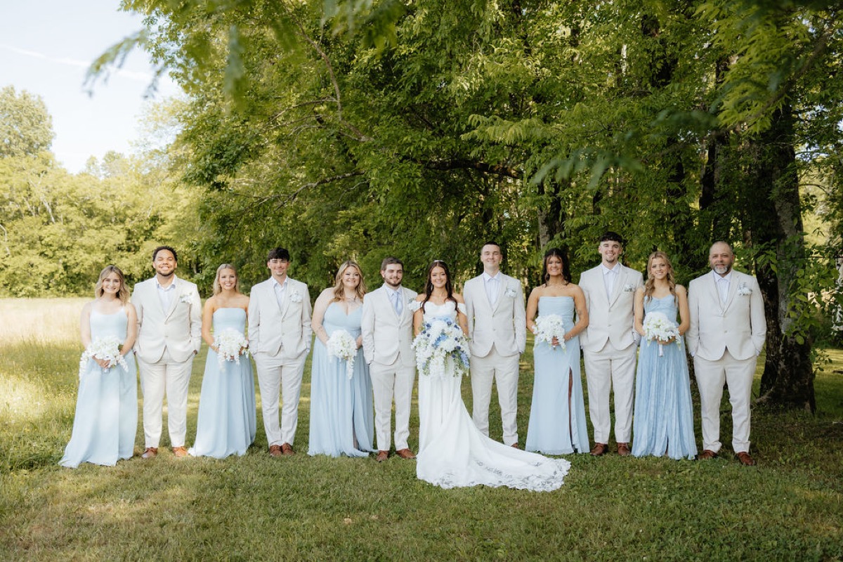 Kylie & Mason pose with bridal party in powder-blue and tan on a green lawn at Covey Creek in spring