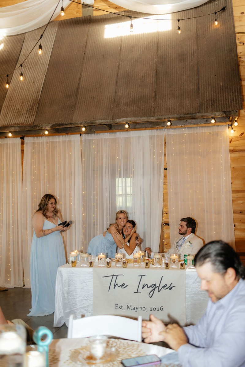 Kylie & Mason at their sweetheart table during toasts in the string-lit indoor reception at Covey Creek