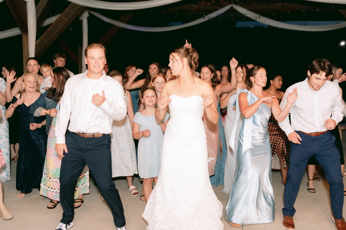 Rachel & Ben dance with guests under string lights at a nighttime patio reception at Covey Creek.