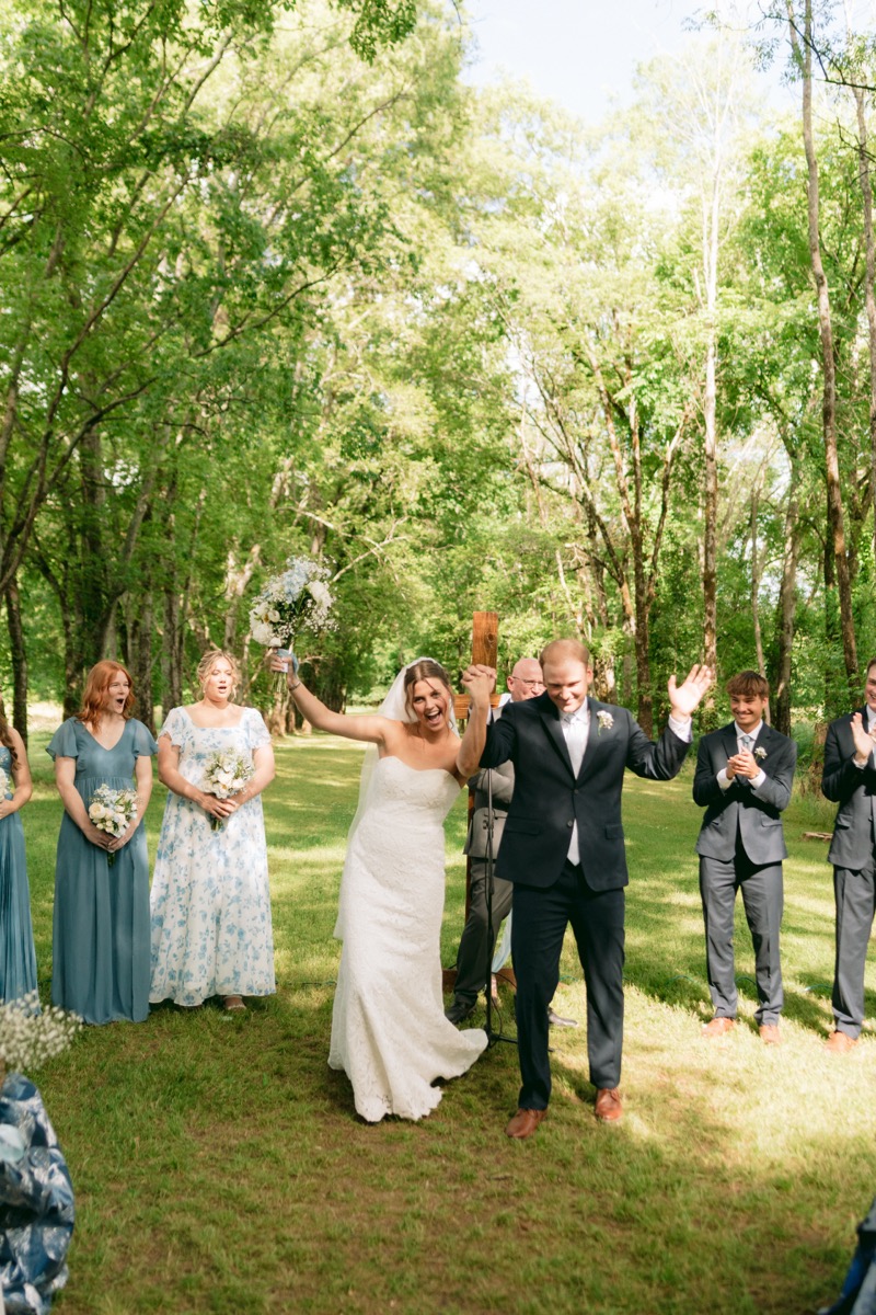 Rachel & Ben recess down the aisle, bouquet raised, under the Tunnel of Love canopy at Covey Creek.