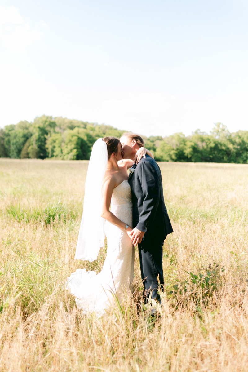 Rachel & Ben share a kiss in a sunlit golden field bordered by green trees at Covey Creek.